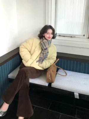 Milk yellow cropped puffer jacket side view showing the relaxed boxy silhouette, front zip closure and hidden hand-warmer pockets on a seated model