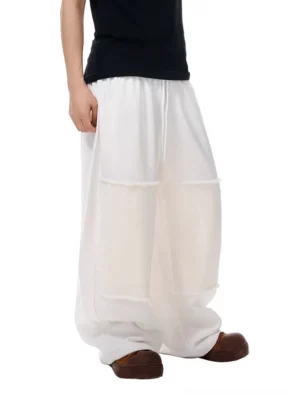 Milky ivory patchwork wide-leg lounge pants with tonal rectangular panels, raw frayed seams, adjustable drawstring waist, and fluid draped streetwear silhouette