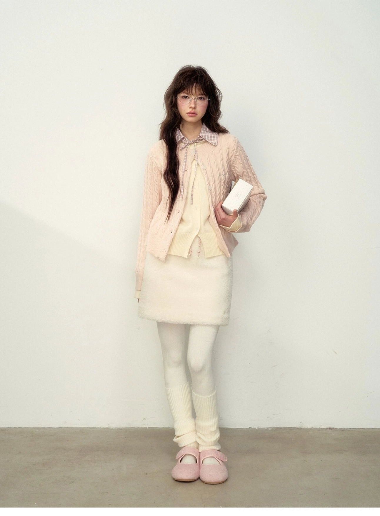 Front view of milky pink cable knit cardigan paired with an off-white skirt and pink loafers