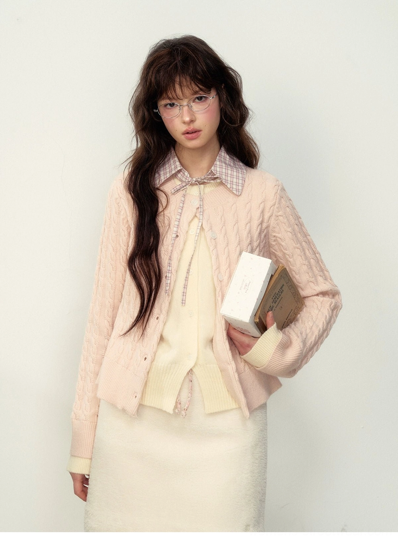 Close-up of milky pink cable knit preppy cardigan texture with plaid collar and bow styling details