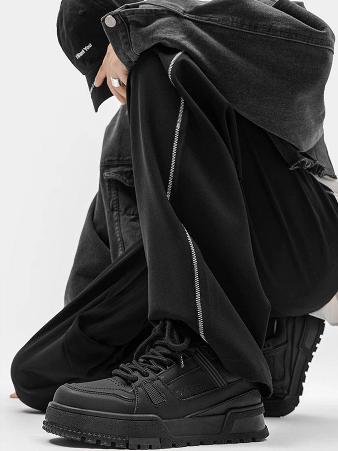 Side view of minimal black platform sneakers worn with wide-leg black side-stripe pants showing the chunky sole and urban streetwear silhouette
