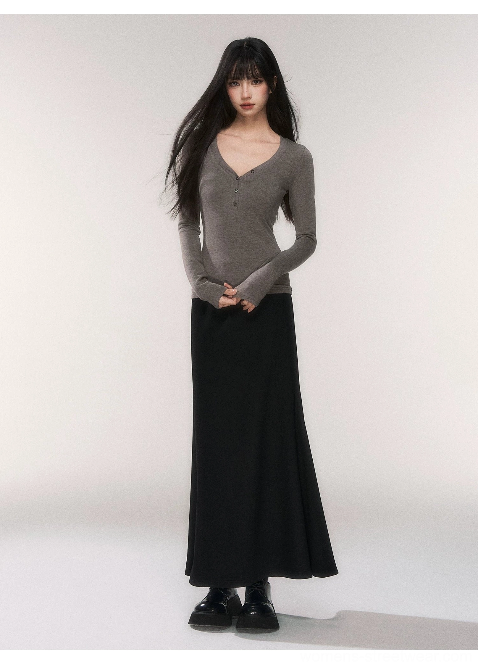 Black fitted knit fishtail maxi skirt in a full length studio outfit with a dark gray V-neck sweater and leather dress shoes