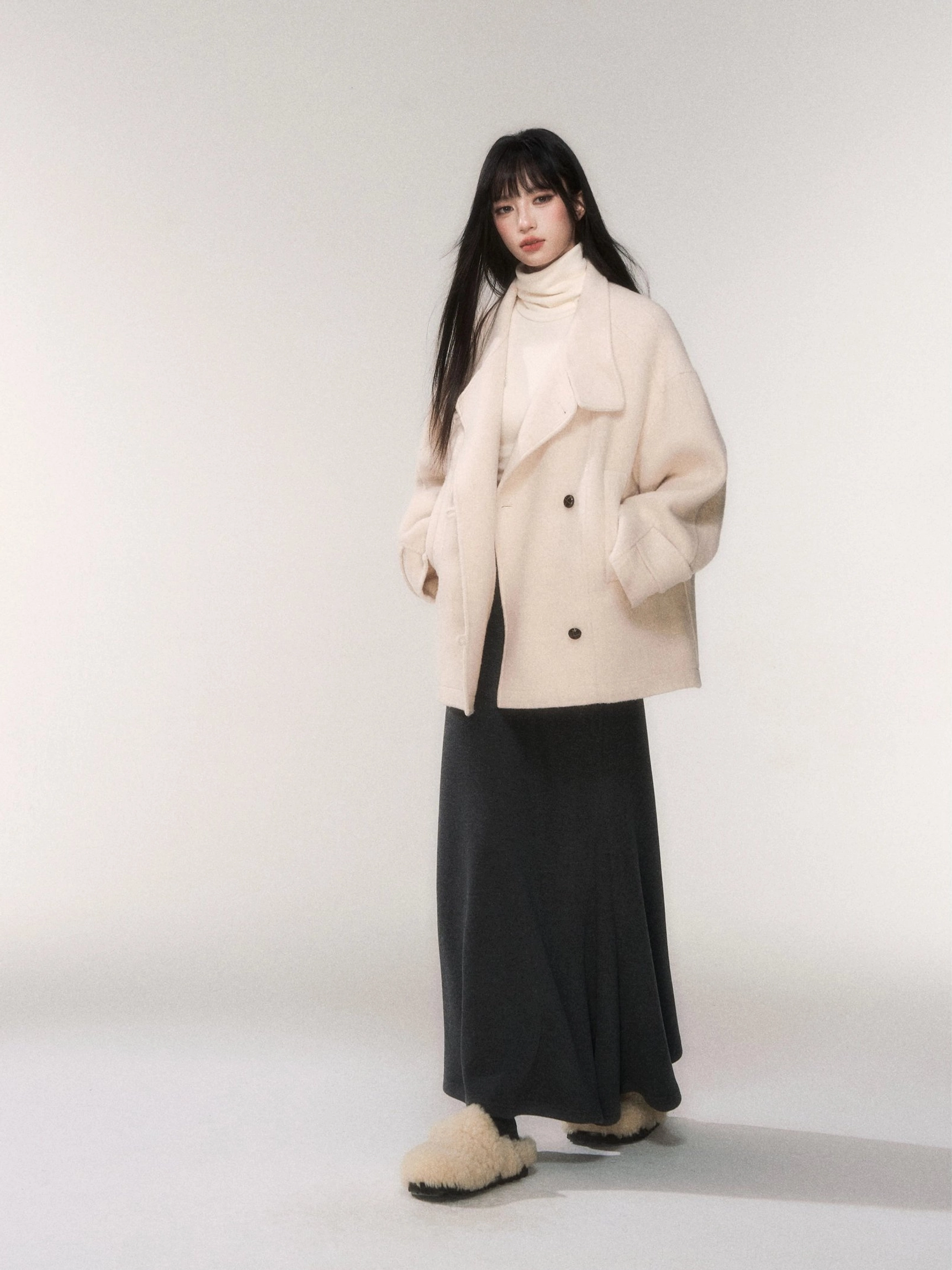 Black knit fishtail maxi skirt paired with a beige double breasted wool coat and ivory turtleneck scarf for elevated winter streetwear