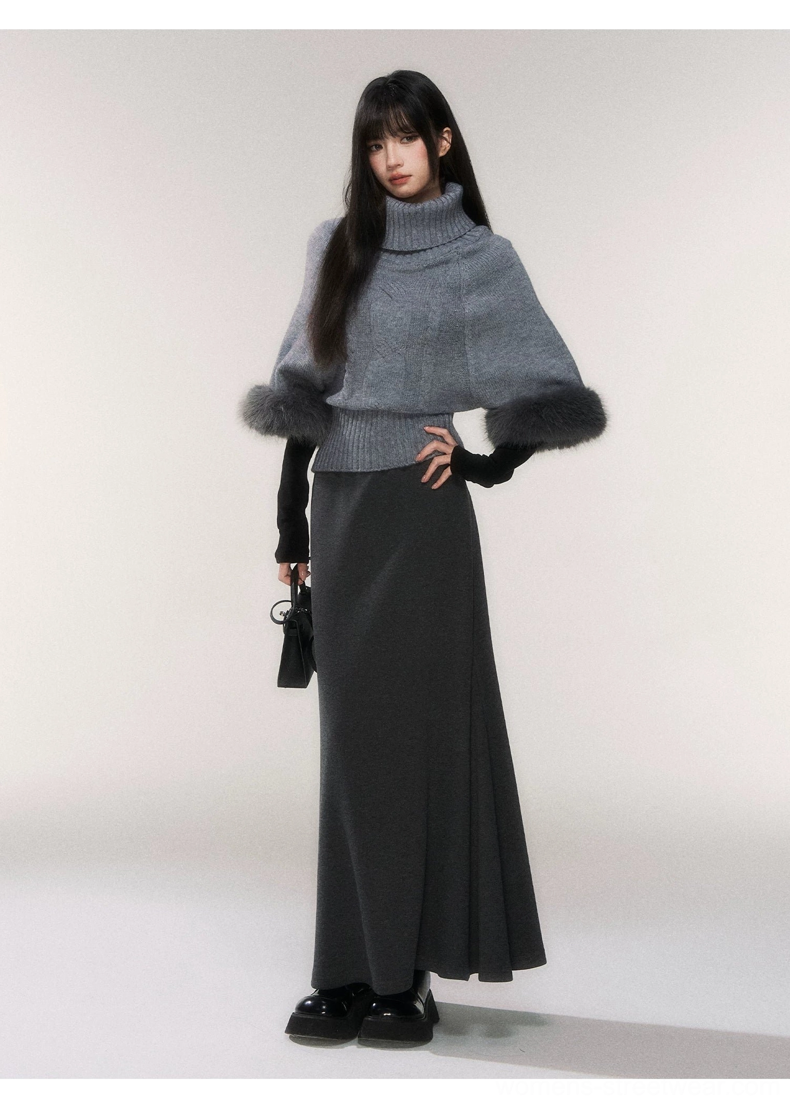 Dark gray long knit fishtail maxi skirt paired with a cape style gray turtleneck sweater with fluffy cuffs and black handbag