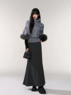 Dark gray minimalist knit fishtail maxi skirt styled with a heather gray turtleneck sweater and black handbag in a studio full body view