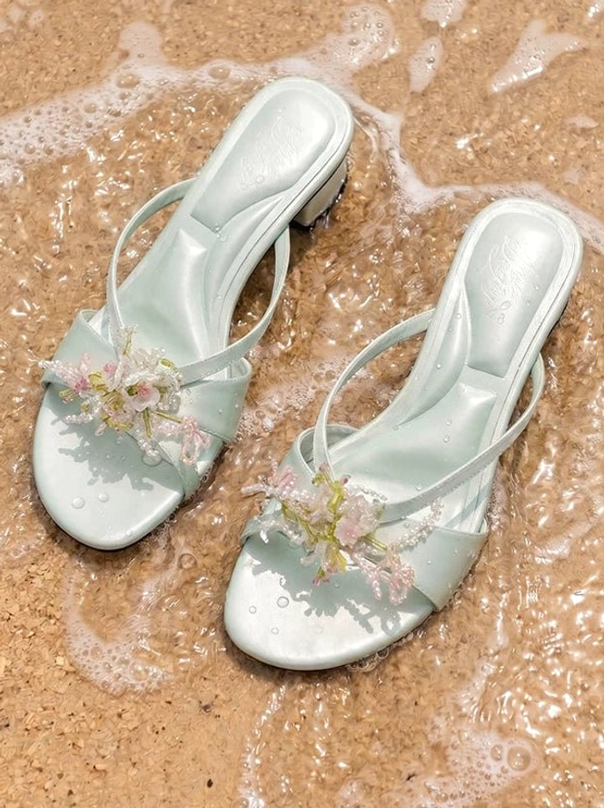 Side view of mint green crossover mules with 3D beaded flower decoration and low block heel on beach sand