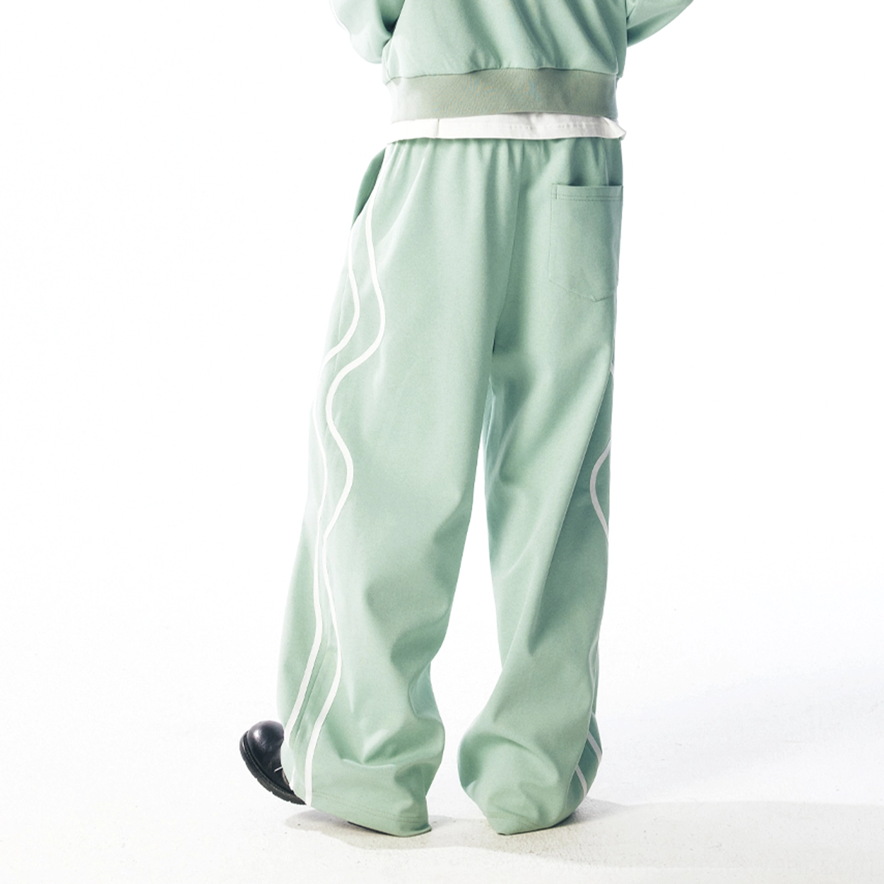 Back three-quarter view of mint green wide-leg track pants with curved white side stripes and rear pocket
