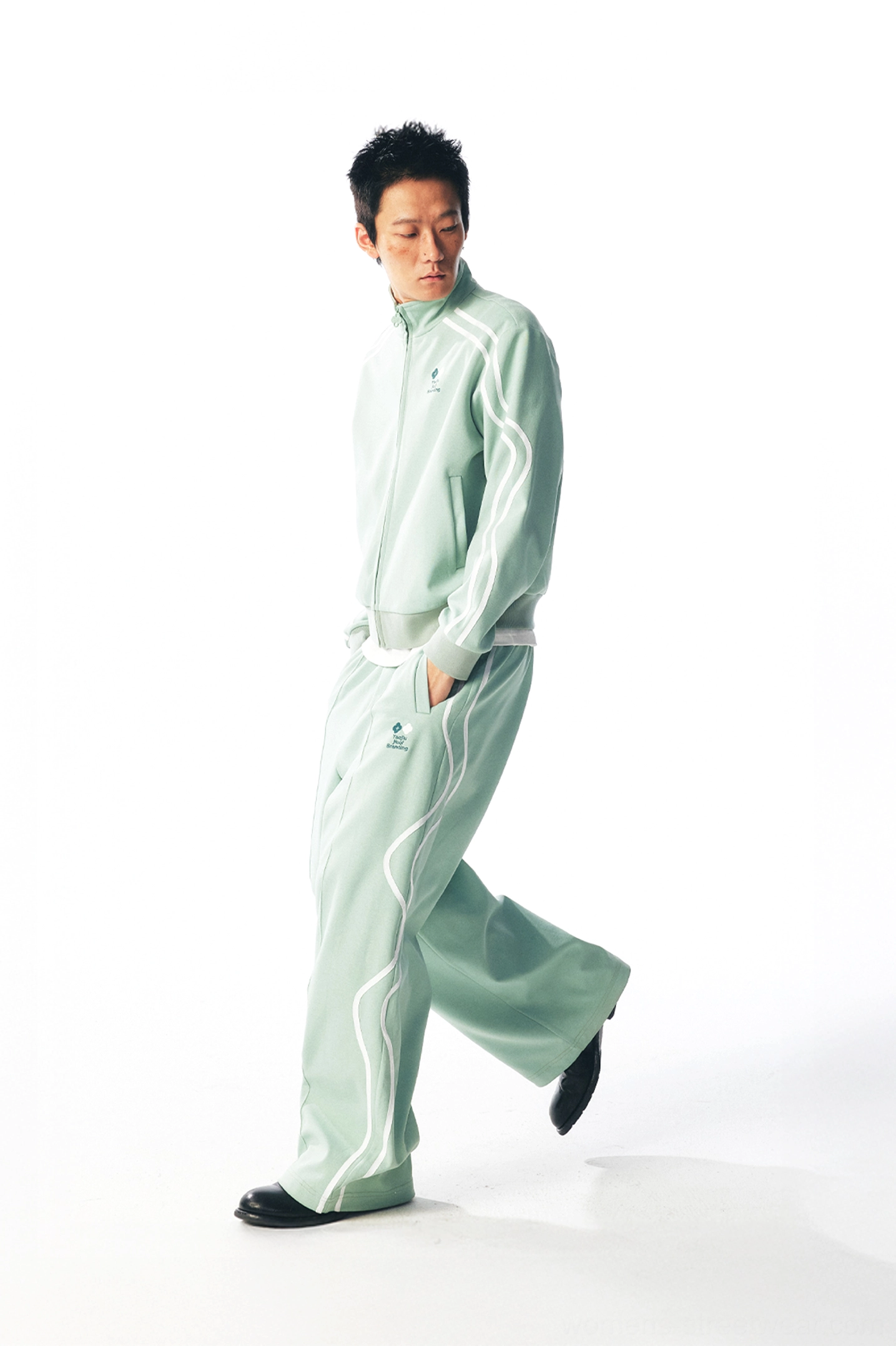 Side walking view of mint green curved stripe track pants with relaxed wide-leg streetwear silhouette