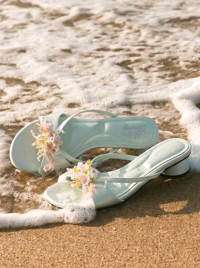 Mint green floral crystal crossover low block heel mules displayed on wet sand by ocean waves