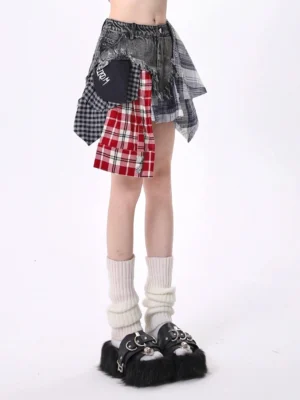 Front close-up of a mixed plaid patchwork denim mini skirt with washed black denim, asymmetric frayed hem, red plaid hanging detail, and Y2K streetwear styling