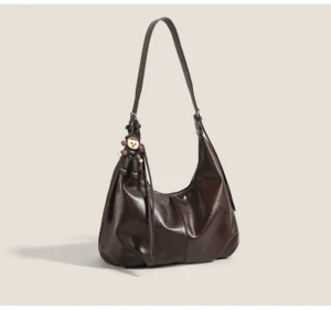 Brown monkey charm crescent hobo shoulder bag shown from the front with a soft glossy faux-leather finish and dangling pendant