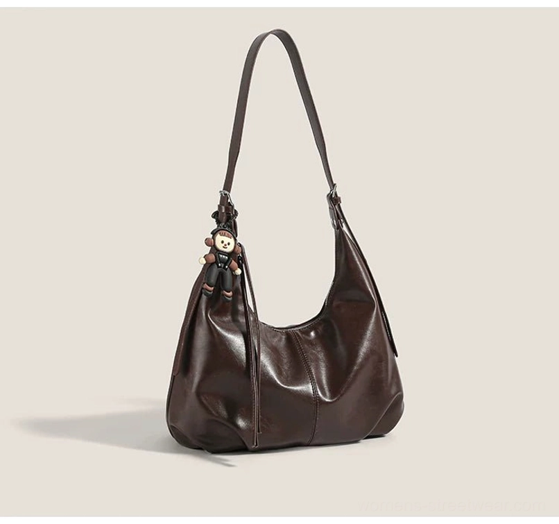 Brown monkey charm crescent hobo shoulder bag shown from the front with a soft glossy faux-leather finish and dangling pendant