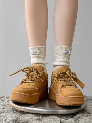 Model wearing wheat monochrome chunky platform sneakers with white crew socks on an industrial metal surface