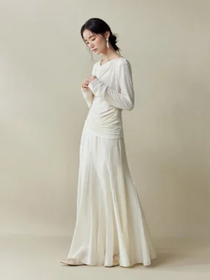 Full body side profile of an Asian female model wearing a Moon White cupro fishtail maxi skirt with structured panel seams and a fitted white knit top