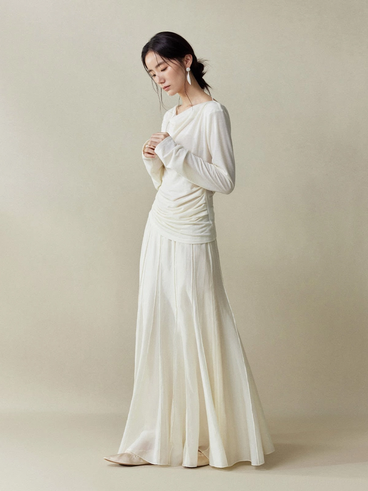 Full body side profile of an Asian female model wearing a Moon White cupro fishtail maxi skirt with structured panel seams and a fitted white knit top