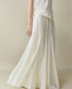 Moon White paneled cupro fishtail maxi skirt shown from a low side angle with flowing drape and vertical seam details styled with a cropped white long sleeve top