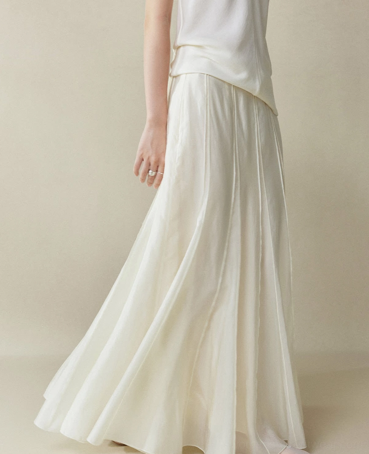 Moon White paneled cupro fishtail maxi skirt shown from a low side angle with flowing drape and vertical seam details styled with a cropped white long sleeve top