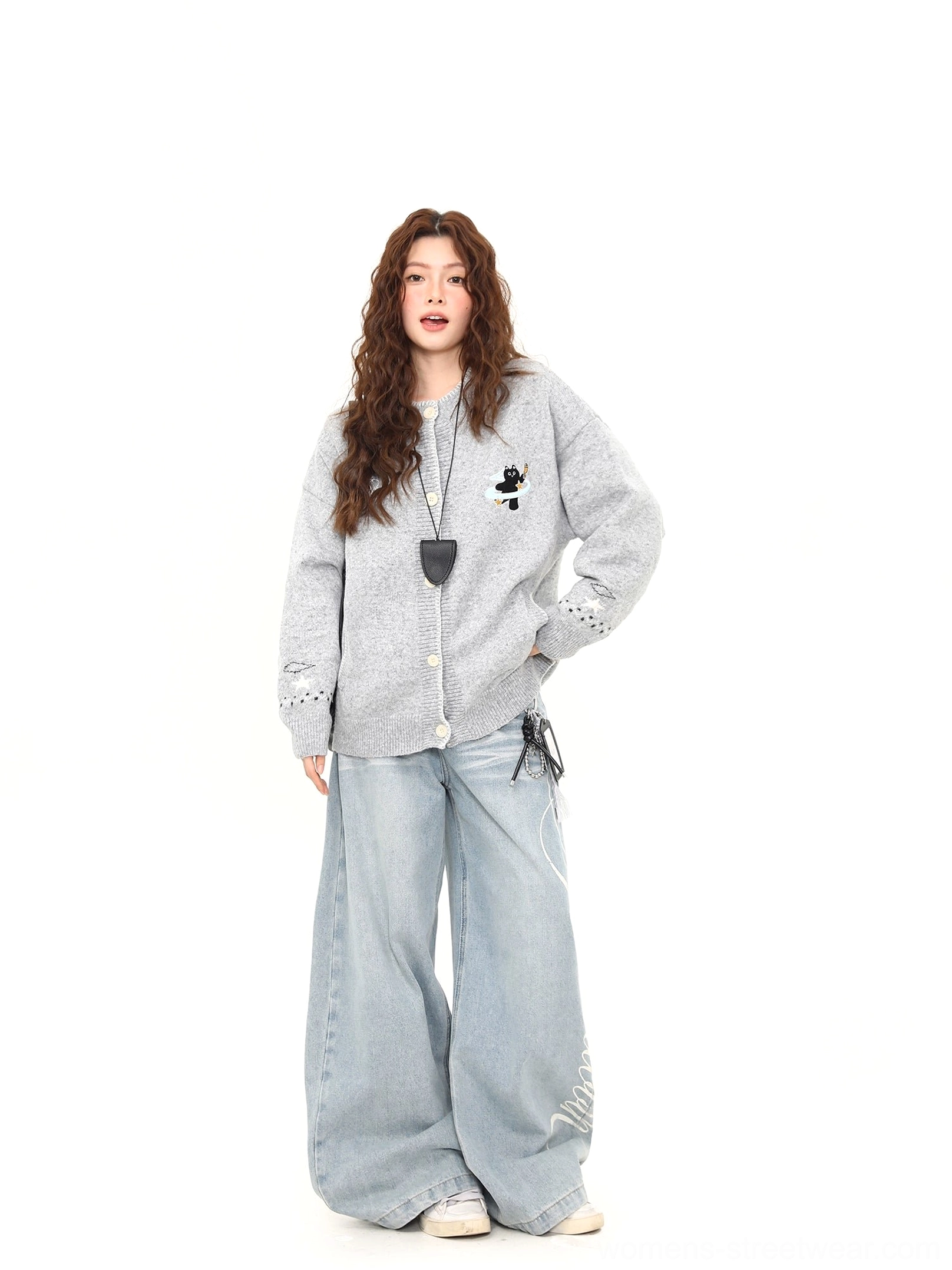 Side three-quarter view of a casual Moonlight Kitty embroidered cardigan with relaxed oversized fit, front buttons, ribbed trims, and light blue wide-leg jeans