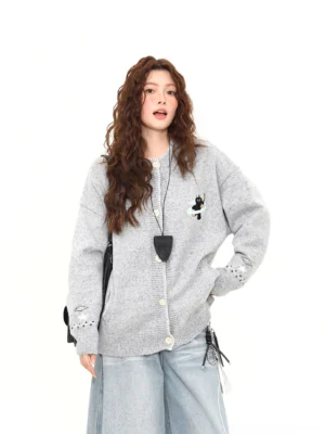 Front three-quarter view of a Moonlight Kitty embroidered oversized knit cardigan in heather grey with black cat flying saucer embroidery, ribbed trims, and wide-leg light blue jeans