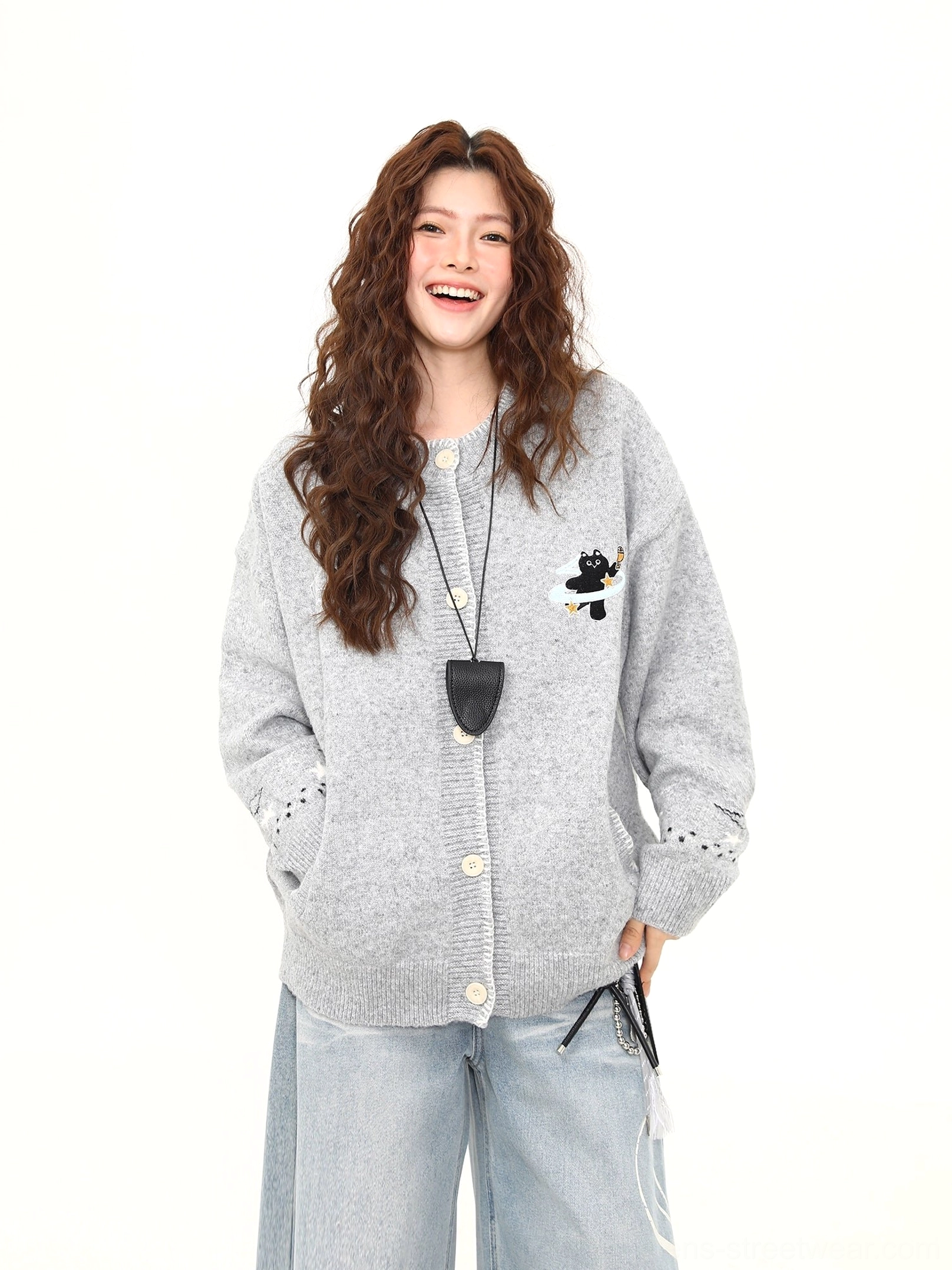 Front three-quarter styling view of a Korean oversized knit cardigan with black cat embroidery, ribbed hem, ribbed cuffs, and contrasting buttons