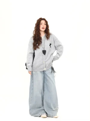 Side three-quarter view of a relaxed oversized Moonlight Kitty knit cardigan with black cat embroidery, ribbed hem and cuffs, styled with wide-leg denim