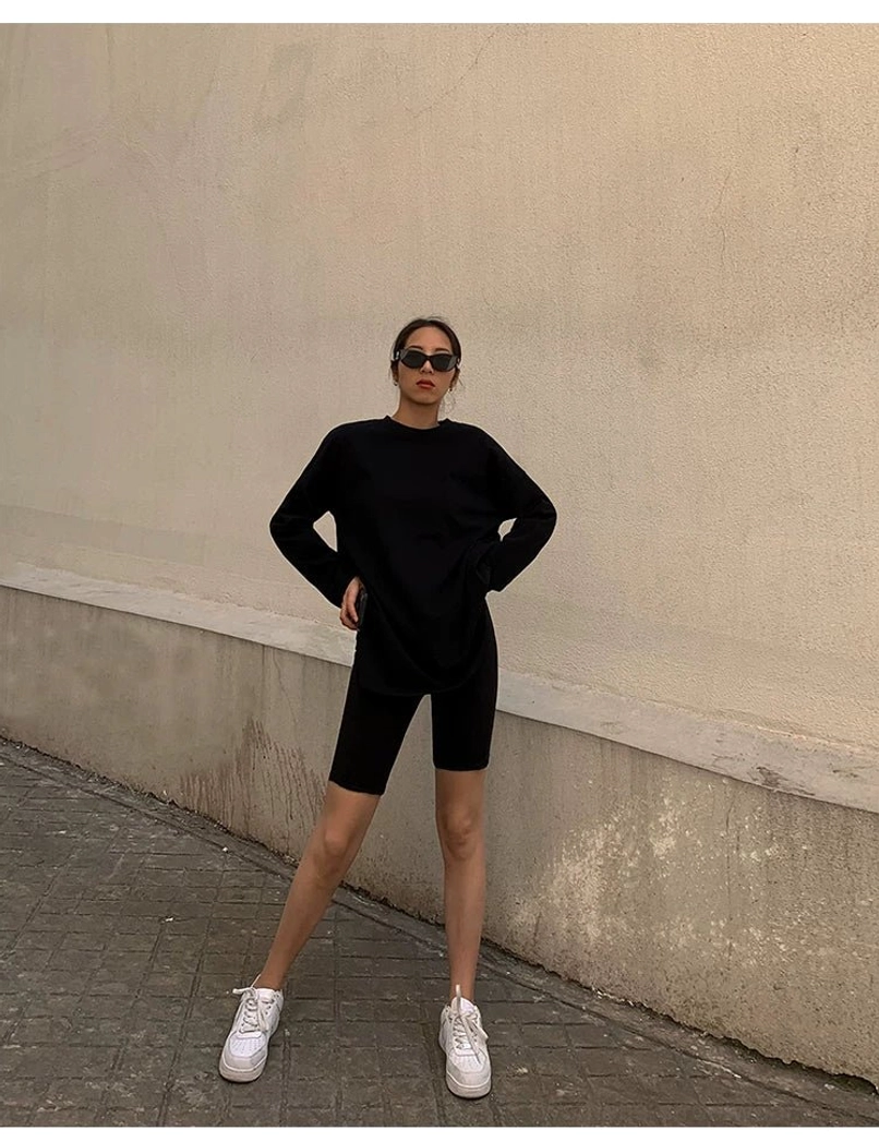 Black oversized long sleeve t-shirt dress worn with black biker shorts and white sneakers, showing a loose mid-thigh silhouette and clean monochrome streetwear styling