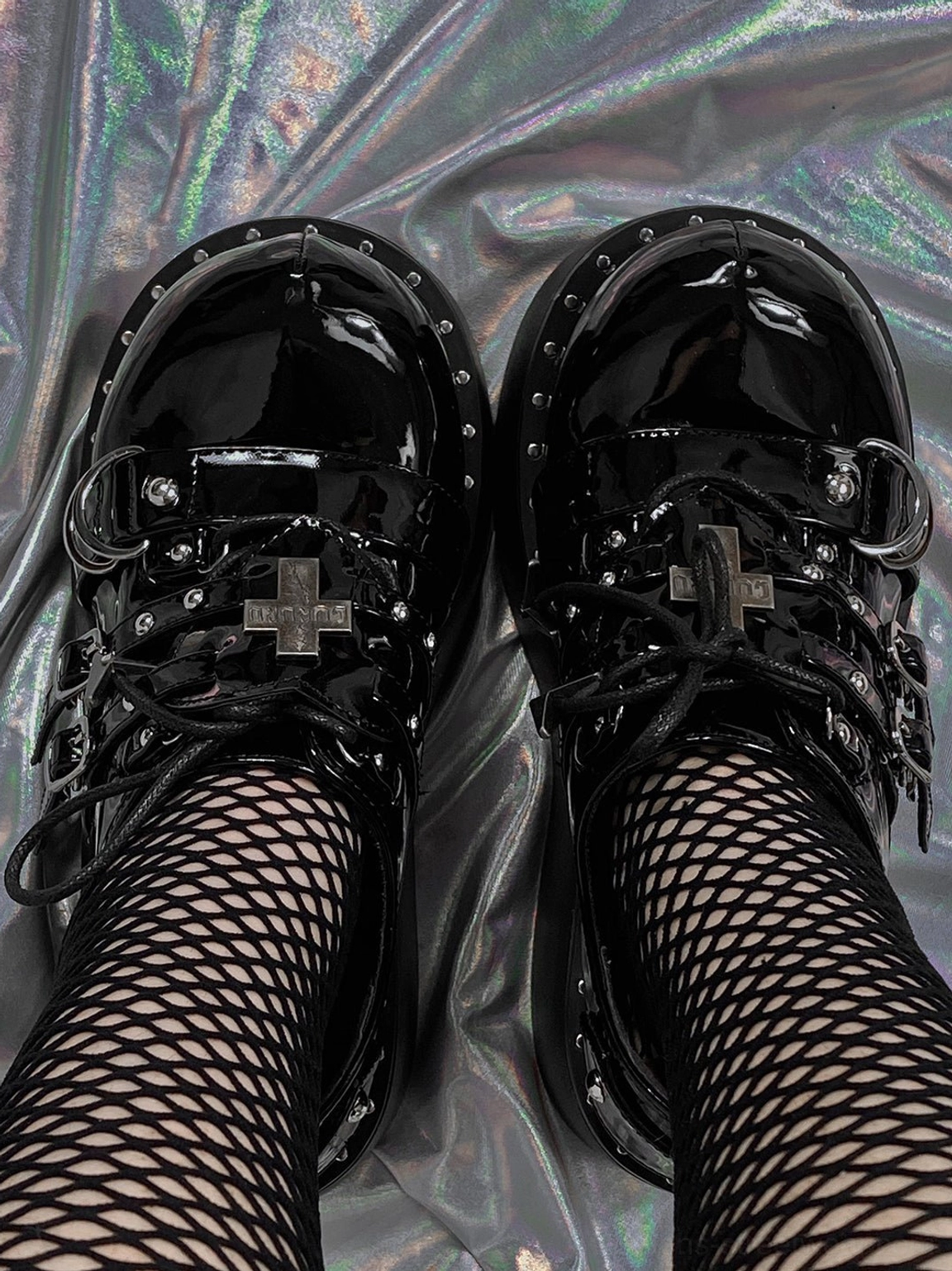 Top view of black patent Gothic platform Mary Jane shoes with buckle straps, cross ornament, and fishnet stockings