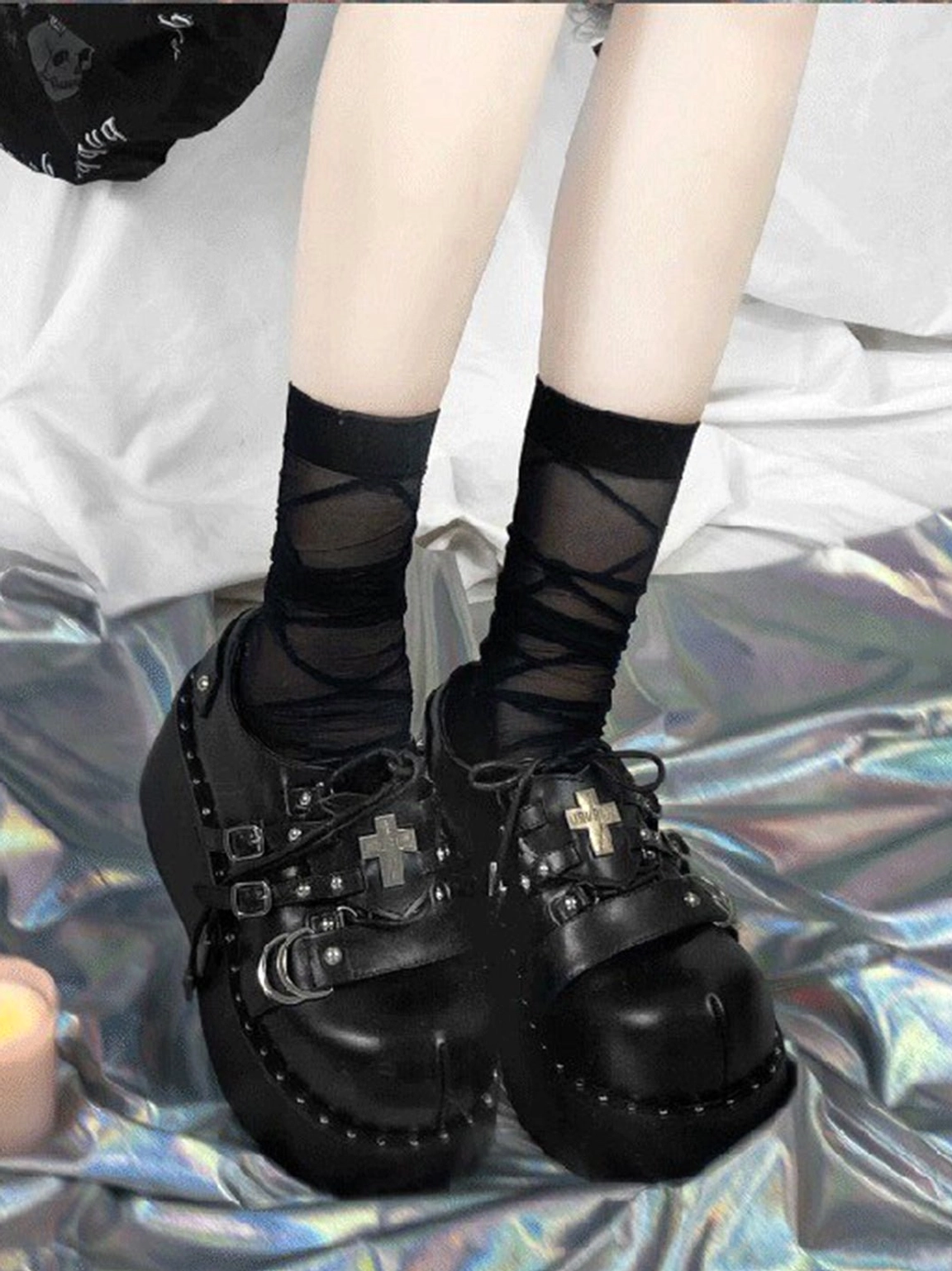 Black patent multi-buckle Gothic platform Mary Jane shoes worn with crisscross black socks on holographic silver fabric