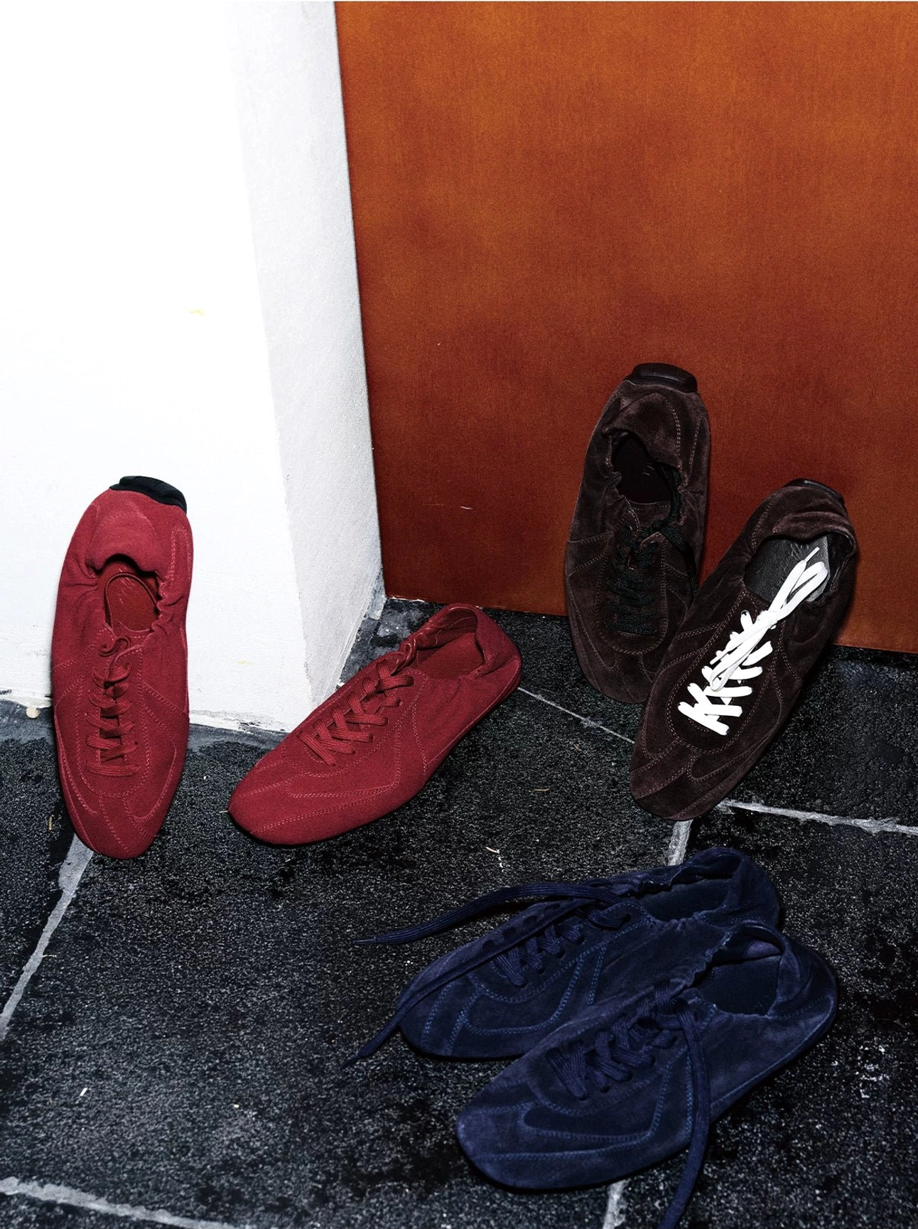 Multi-color suede minimalist lace-up sneakers in red, dark brown, and navy blue arranged in an indoor lifestyle setting