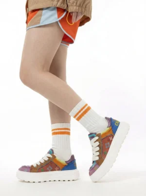 Model wearing multicolor embossed platform skate sneakers with striped socks and orange shorts on a white studio background