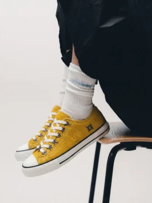 Mustard yellow cowhide low-top sneakers worn with printed white crew socks in a casual streetwear outfit from a top-down view