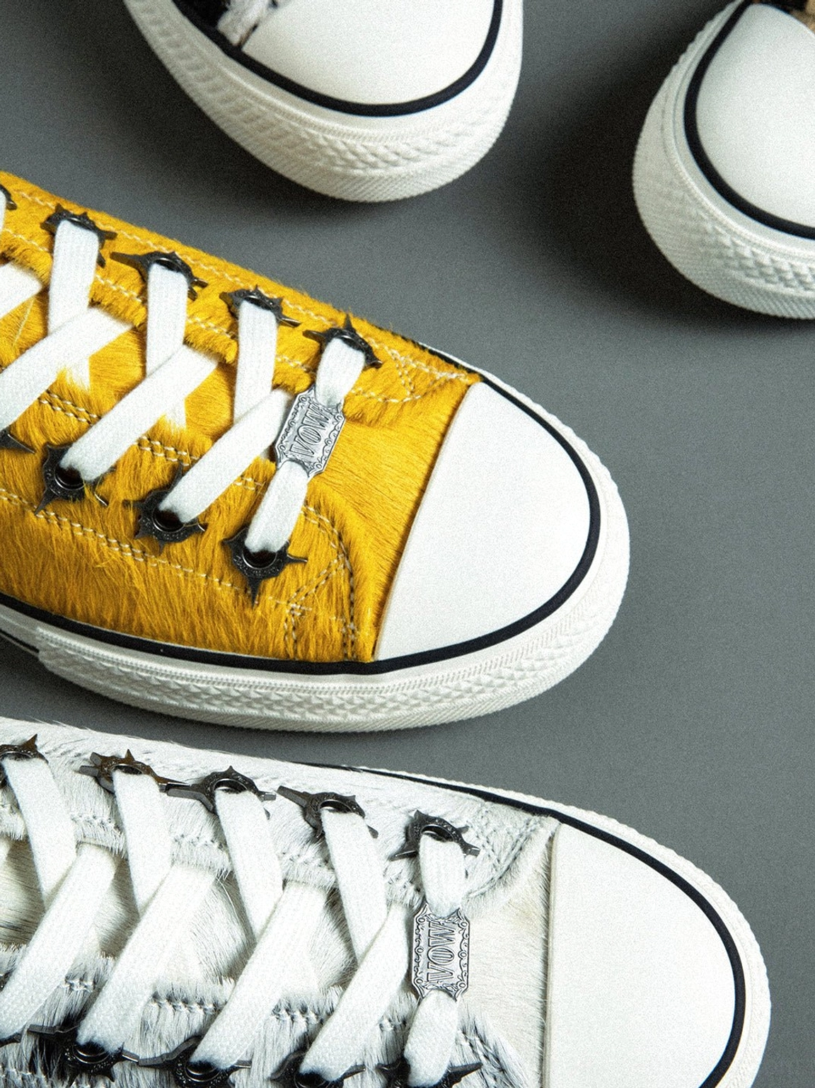 Close-up detail of mustard yellow cowhide sneakers showing fluffy textured leather, metal lace hardware, and white rubber toe cap