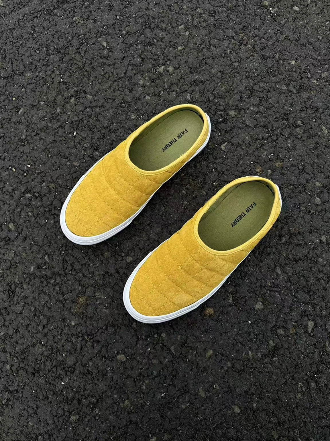 Top view of a pair of mustard yellow quilted backless sneaker mules placed on urban asphalt pavement
