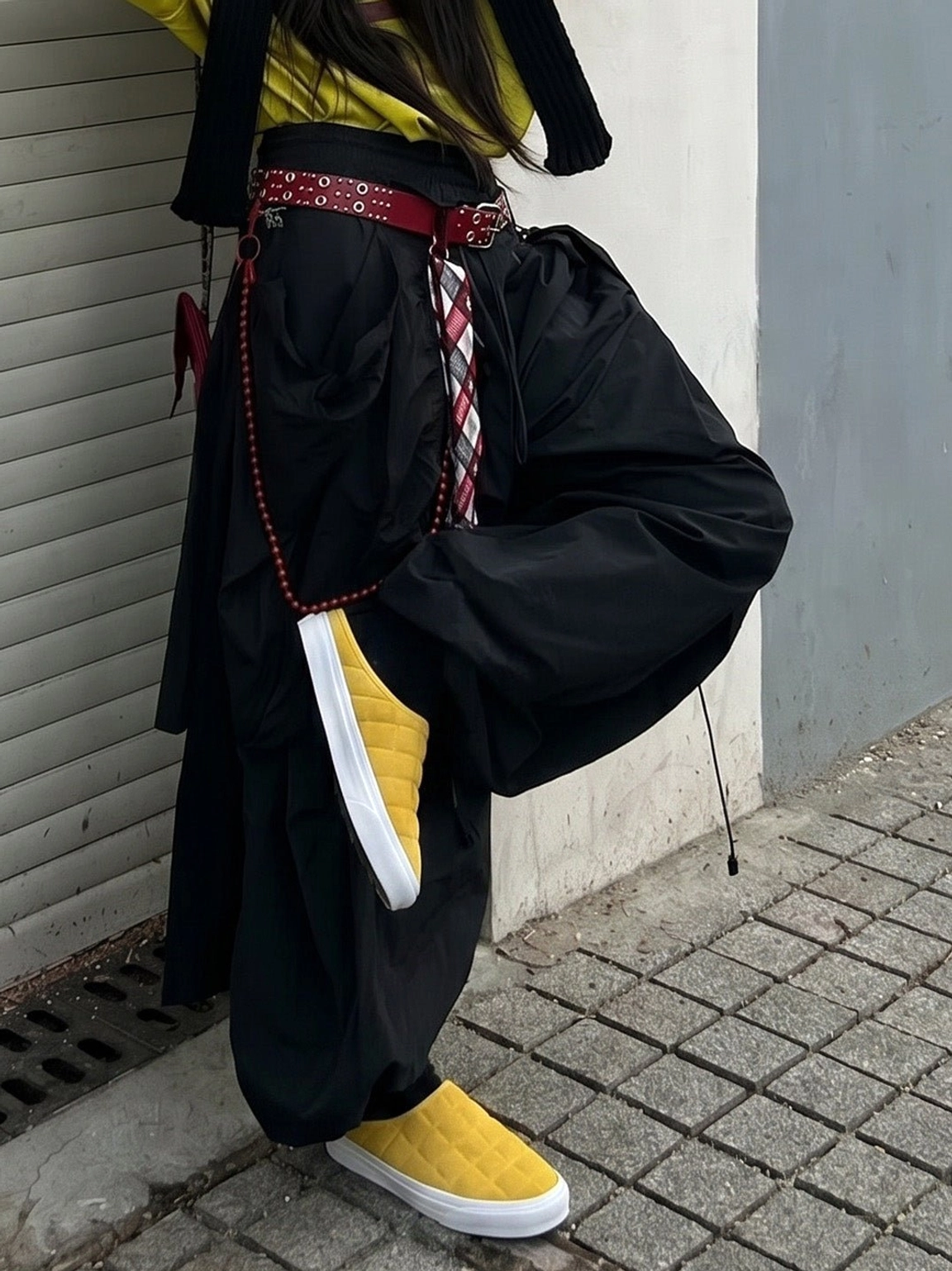 Mustard yellow quilted backless sneaker mules styled with wide-leg pants against an urban roller shutter