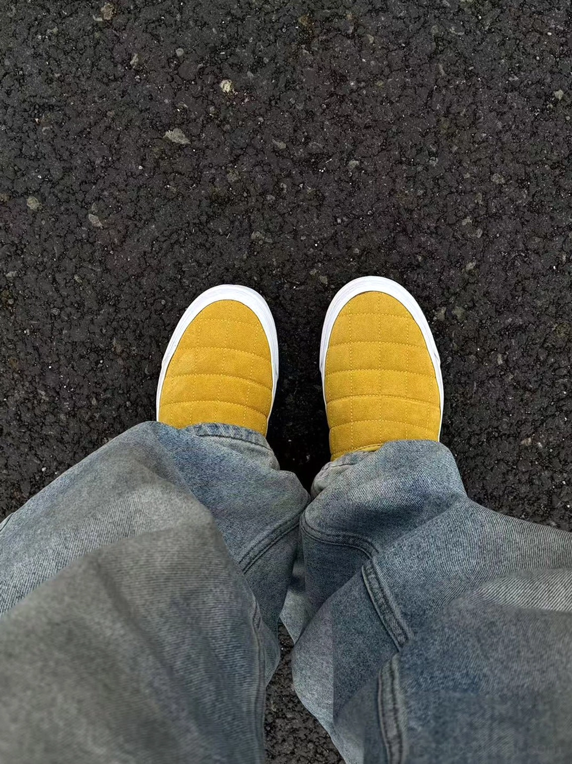 Top-down view of both mustard yellow quilted slip-on sneaker mules worn with relaxed blue jeans