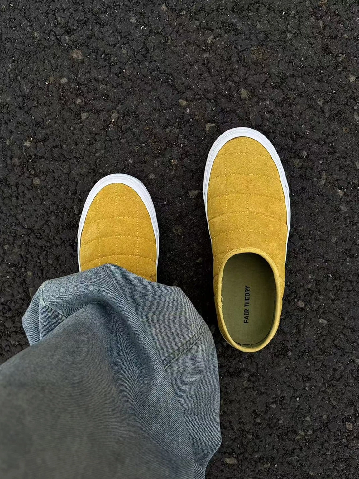 First-person view of mustard yellow quilted slip-on sneaker mules worn with blue denim jeans outdoors