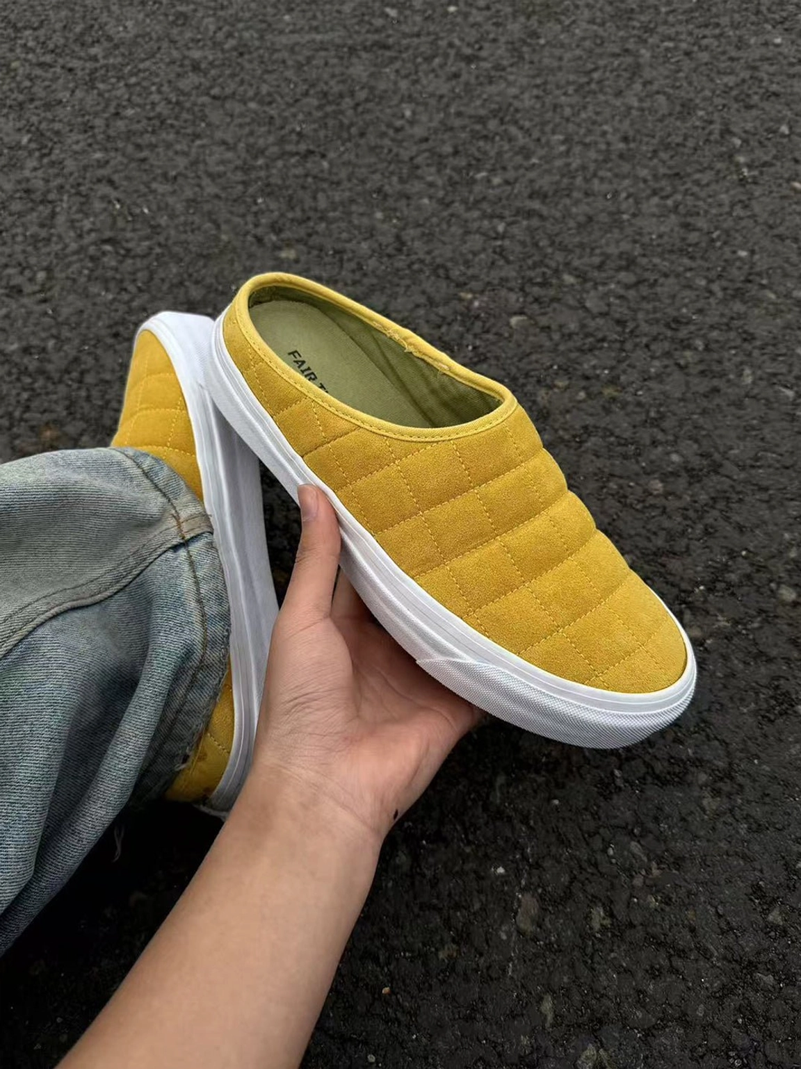 Mustard yellow quilted sneaker mule held in hand beside matching mule worn with casual denim pants
