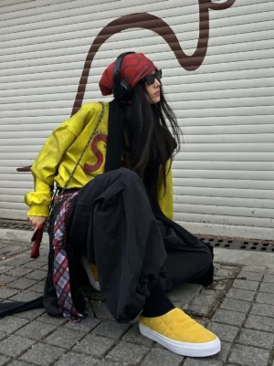 Mustard yellow quilted sneaker mules worn with wide black pants in a colorful urban streetwear outfit