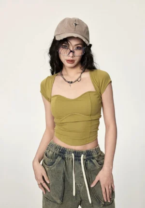 Mustard yellow ribbed twist open back crop top shown from the front with sweetheart neckline, fitted silhouette, cropped hem, layered necklace, and retro denim