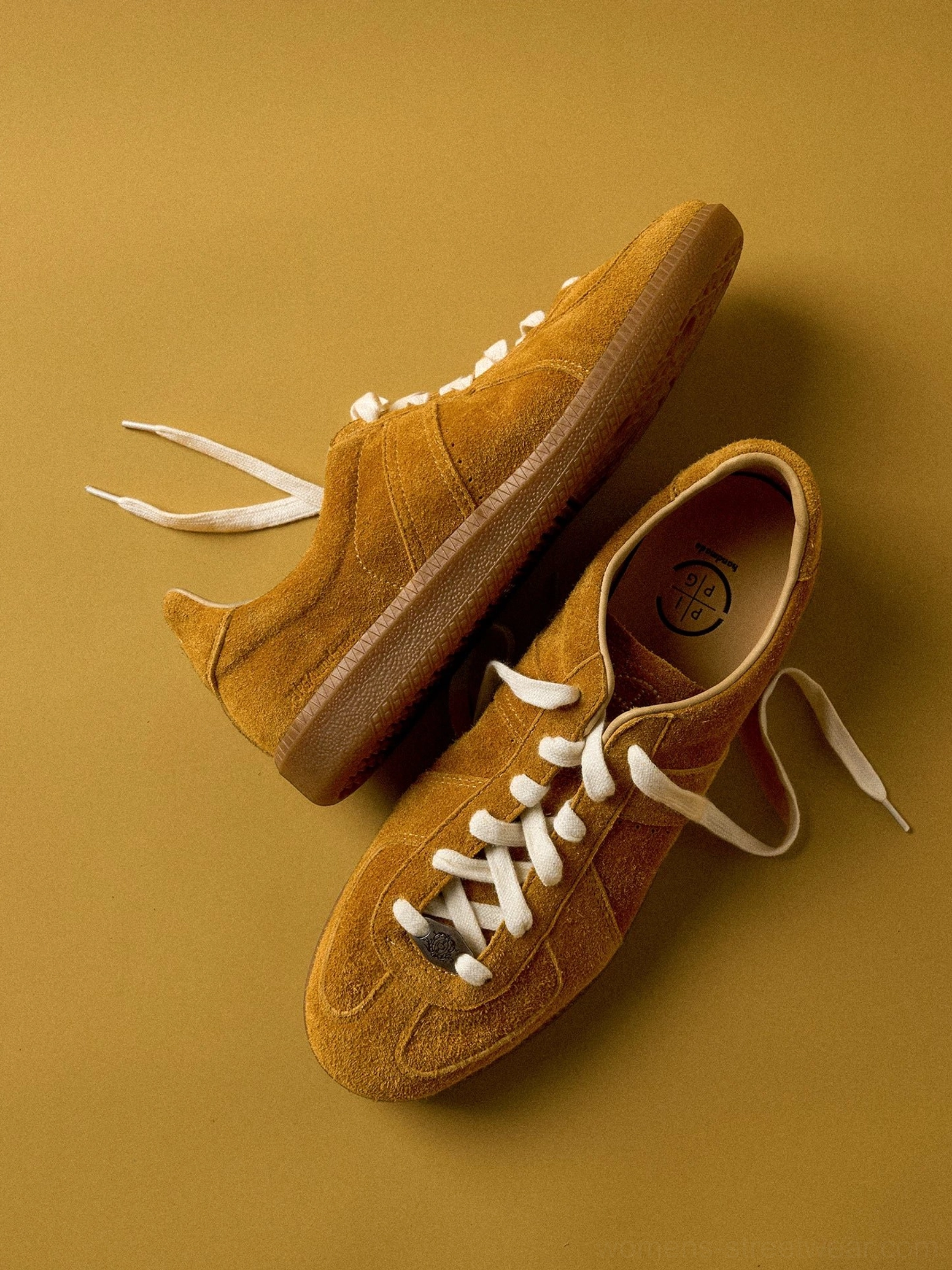 Mustard yellow suede heritage leather sneakers with off-white laces, classic low-top trainer shape, and gum rubber sole