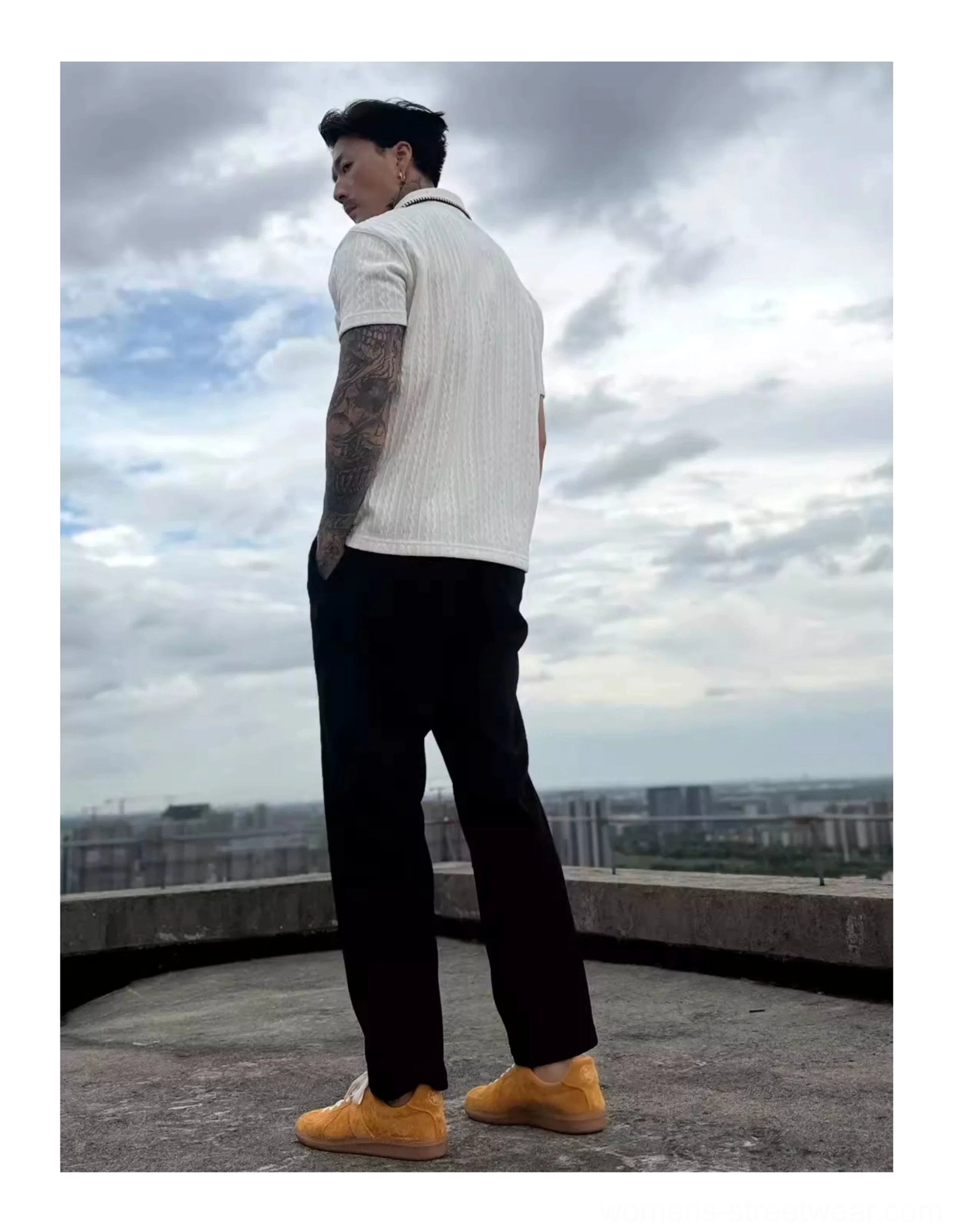 Side profile of mustard yellow suede heritage sneakers styled with casual tailored clothing against a modern city skyline