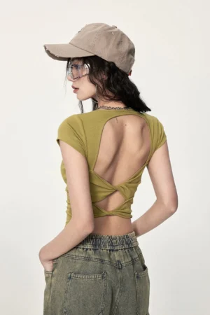 Mustard yellow twisted open back cropped streetwear top shown from the rear with ribbed fabric, twisted cutout detail, cropped hem, and wide leg jeans