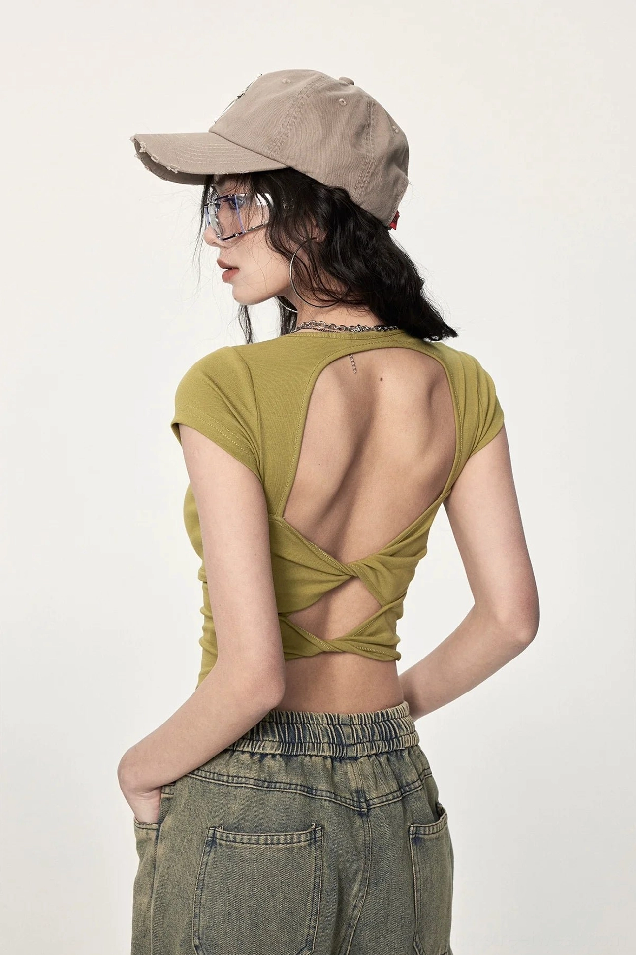 Mustard yellow twisted open back cropped streetwear top shown from the rear with ribbed fabric, twisted cutout detail, cropped hem, and wide leg jeans