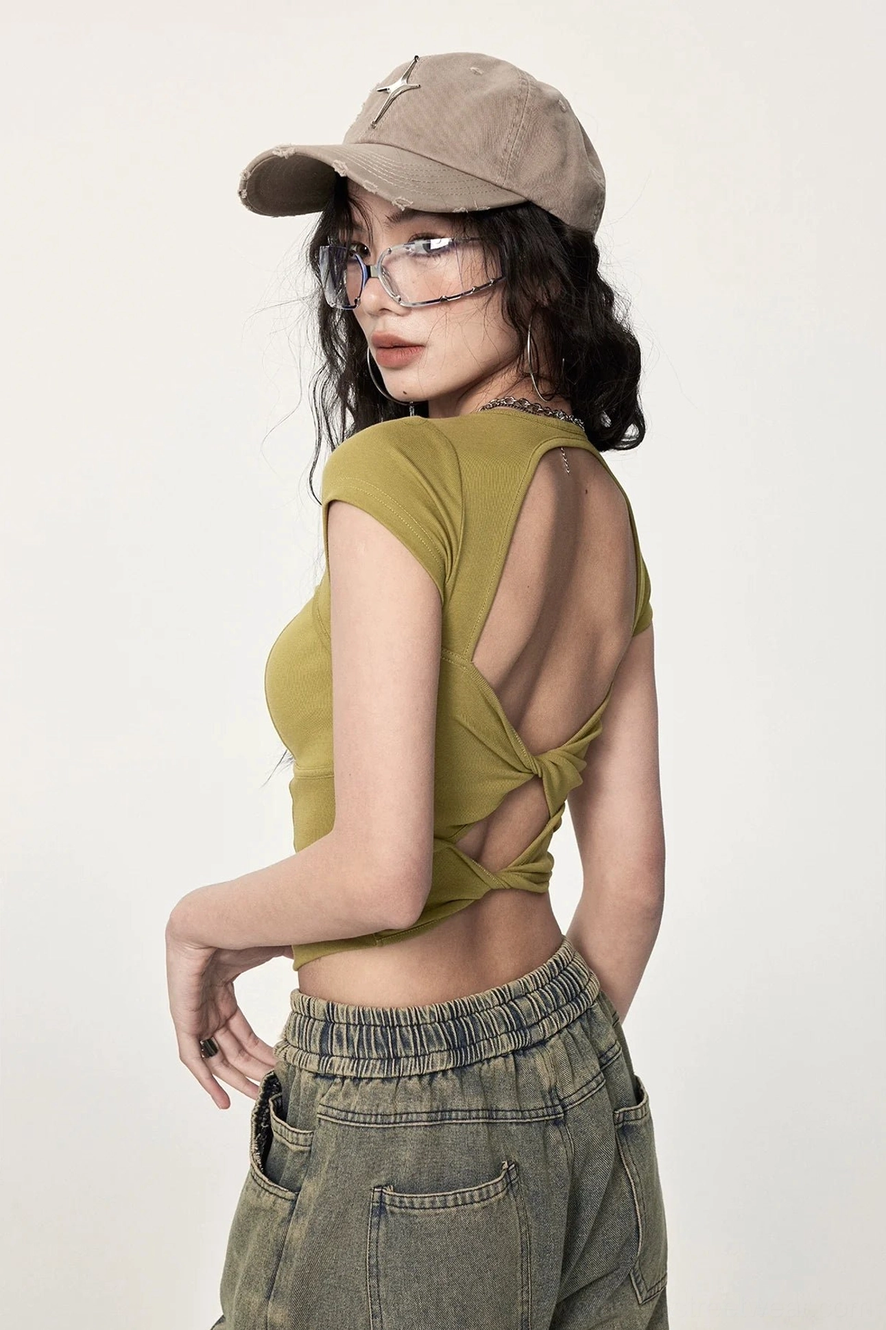 Side rear view of mustard yellow twisted open back cropped tee with ribbed knit texture, short sleeves, bare waist, and retro denim styling