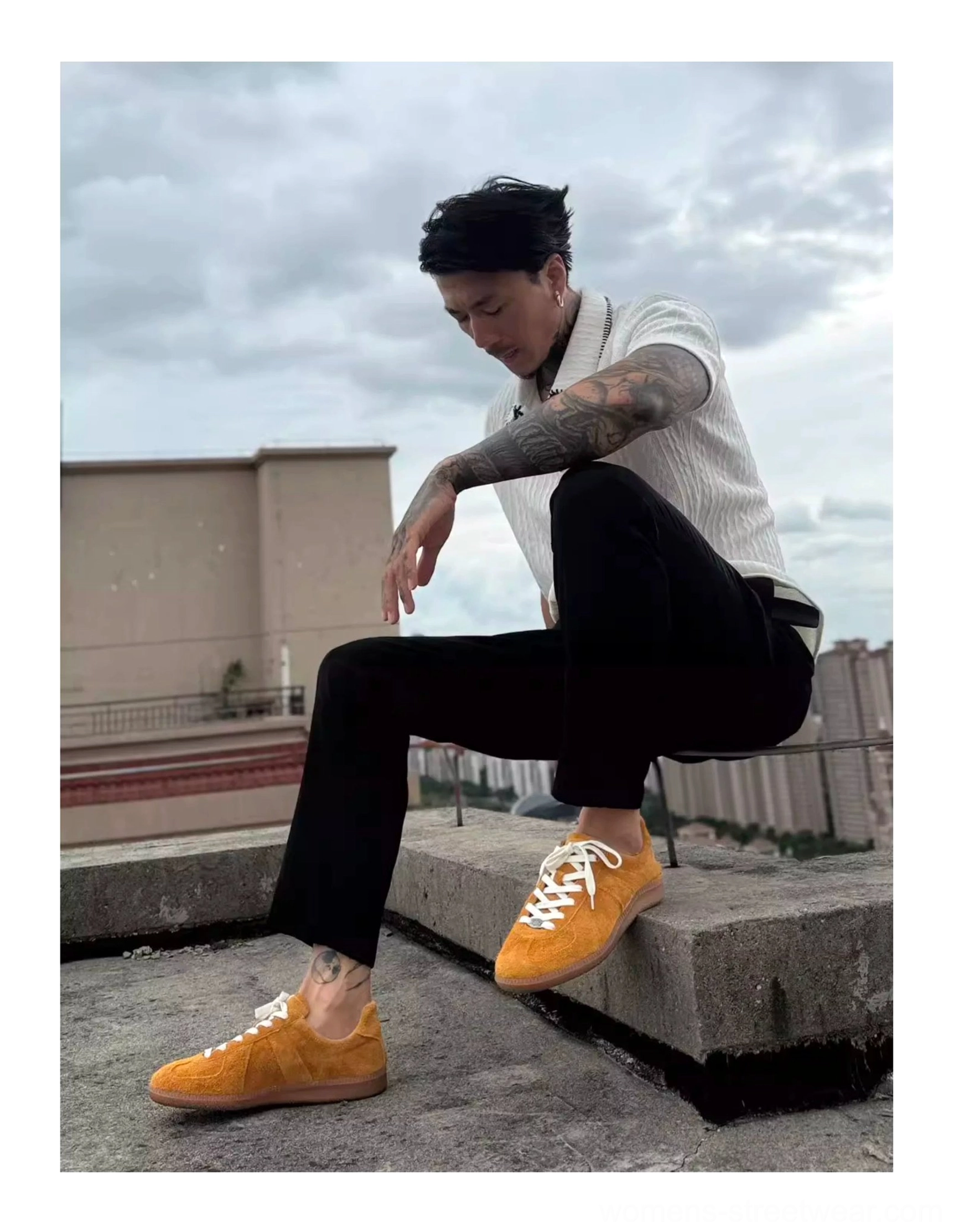 Mustard yellow vintage leather suede sneakers worn in a relaxed urban outfit while seated on a concrete rooftop ledge