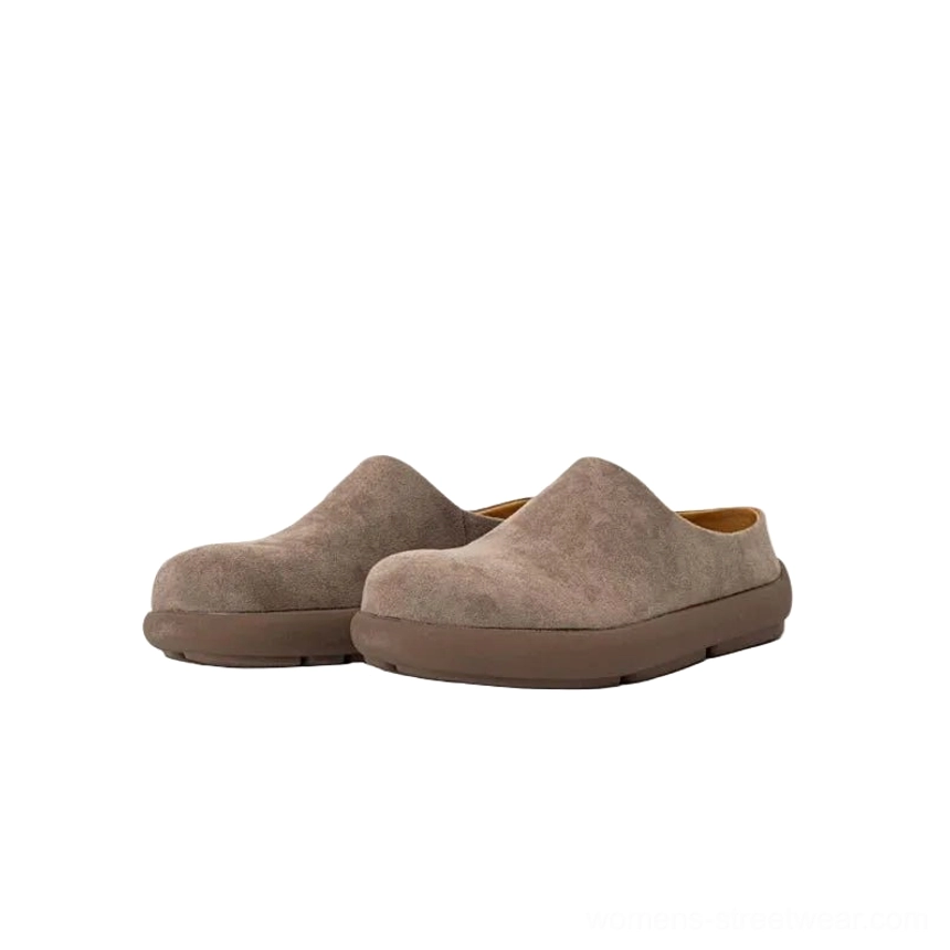 Muted taupe suede mule clogs shown from a side-front angle, highlighting the matte neutral upper, open heel, rounded toe, and brown rubber outsole