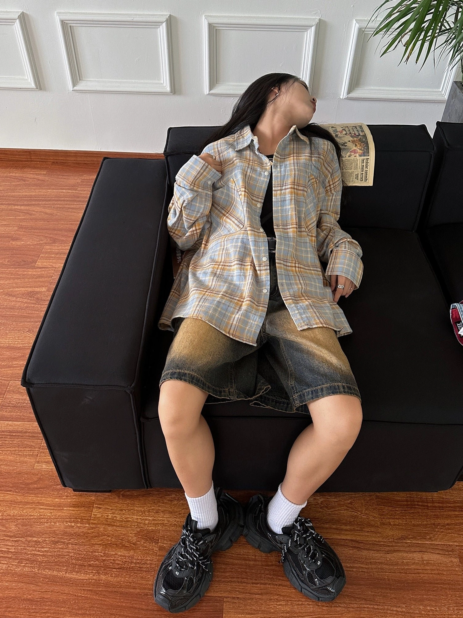 Woman sitting on a sofa wearing a muted yellow blue plaid flannel shirt with vintage denim shorts