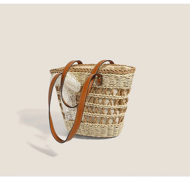 Back three-quarter view of a natural woven basket tote with horizontal straw stripes, long brown straps, and lace bow detail