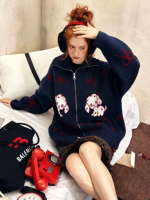 Navy blue oversized puppy print zip-up sweater with red bow and zigzag jacquard details styled with brown ruffled shorts on a vintage bed