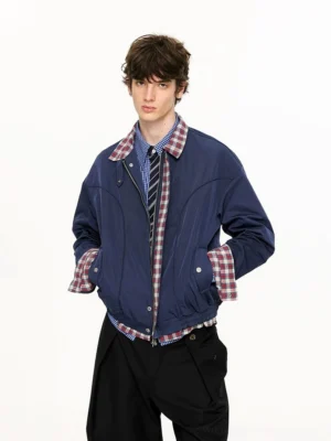Male model wearing a navy blue plaid-lined Harrington jacket with checked shirt striped tie and wide-leg black trousers